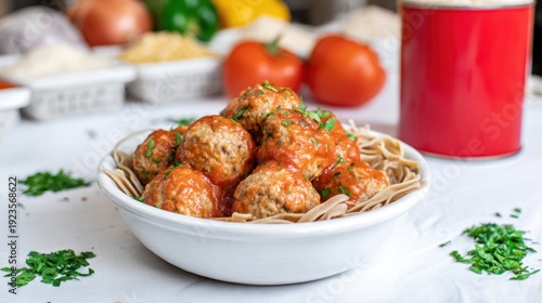 Close-up of meatballs in tomato sauce with pasta, surrounded by ingredients on white surface
