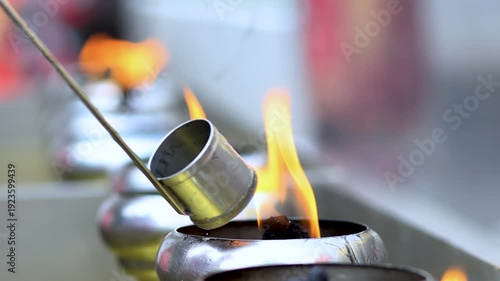 Pouring oil into metal candle cup with burning flame. Ritual and meditation atmosphere symbolizing faith, spirituality, hope, and peaceful ambiance