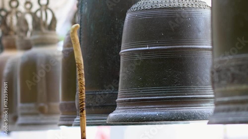 Wooden striker hitting metal temple bell. Peaceful ritual atmosphere symbolizing faith, meditation, Buddhism, and cultural tradition