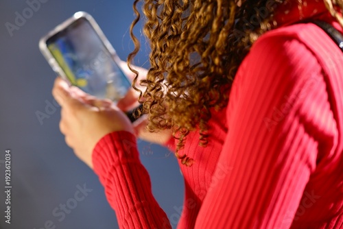 Woman Using Smartphone With Curly Hair Wearing Red Sweater IndoorsDays