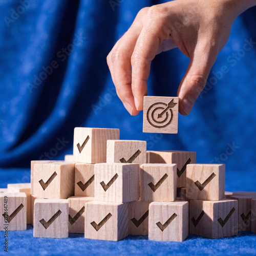 Goal achievement and business success concept with hand placing wooden block with target icon among check mark blocks on blue background for task management, strategy planning, and project milestone