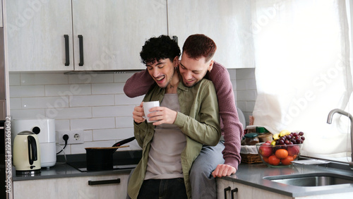 Quadro su tela Young gay couple sharing a loving moment in the kitchen during breakfast