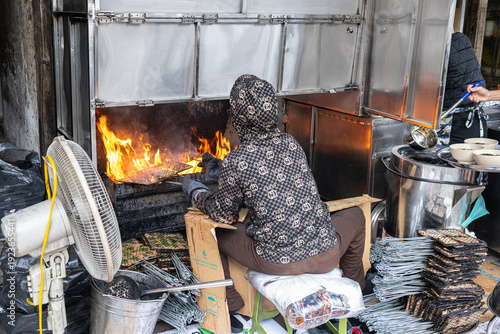 Street vendor grilling small items on metal racks over a large fire in an outdoor market hanoi vietnam