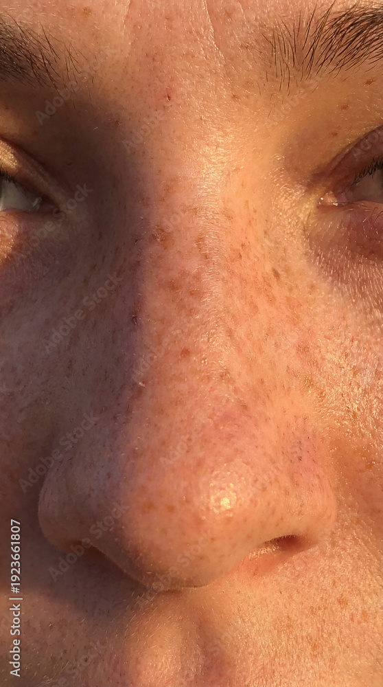 Naklejka premium Young person looks at camera with freckles on face. Soft light reflects on smooth skin. Setting suggests outdoor activity during sunset. Concept of beauty, youth, wellness