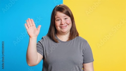 Smiling young woman waving hello with a friendly gesture on a colorful background.