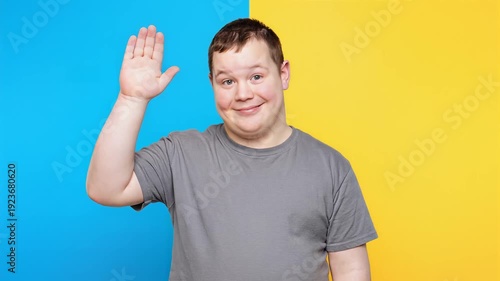Friendly man waving hello with a smile on a vibrant blue and yellow background, expressing a warm greeting and positive emotion.