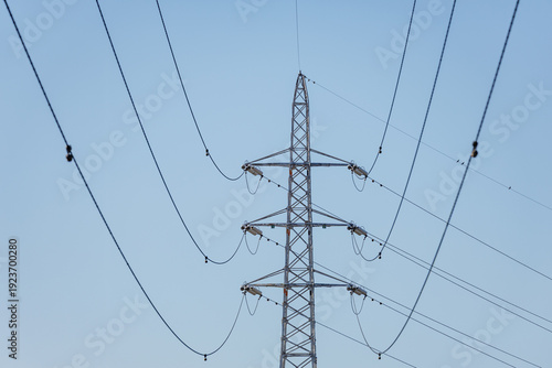 High-voltage lattice transmission tower supporting multiple levels of power lines stretching in catenary curves across clear blue sky.