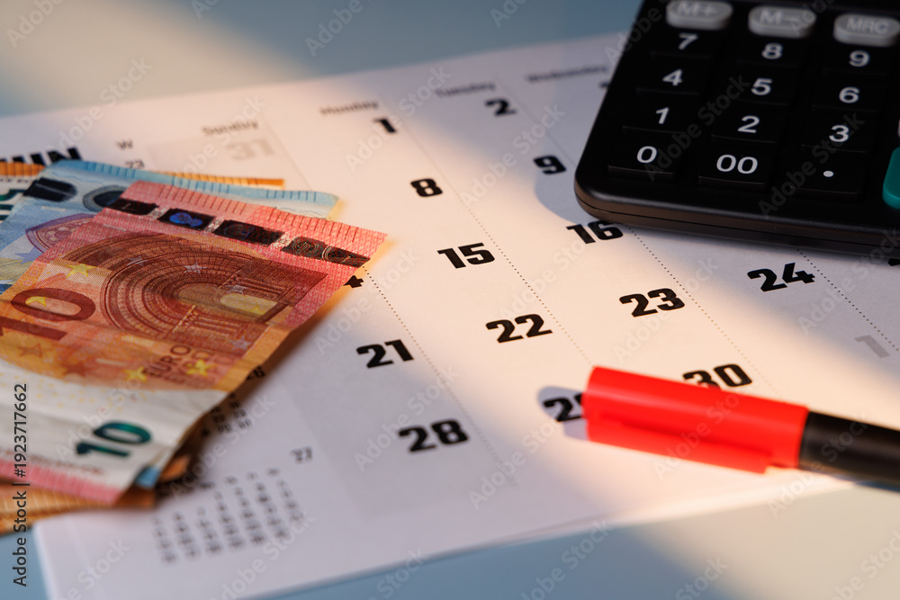 Fototapeta premium Euro banknotes on a desk calendar with office supplies and a digital calculator in warm solar light for professional tax concepts.