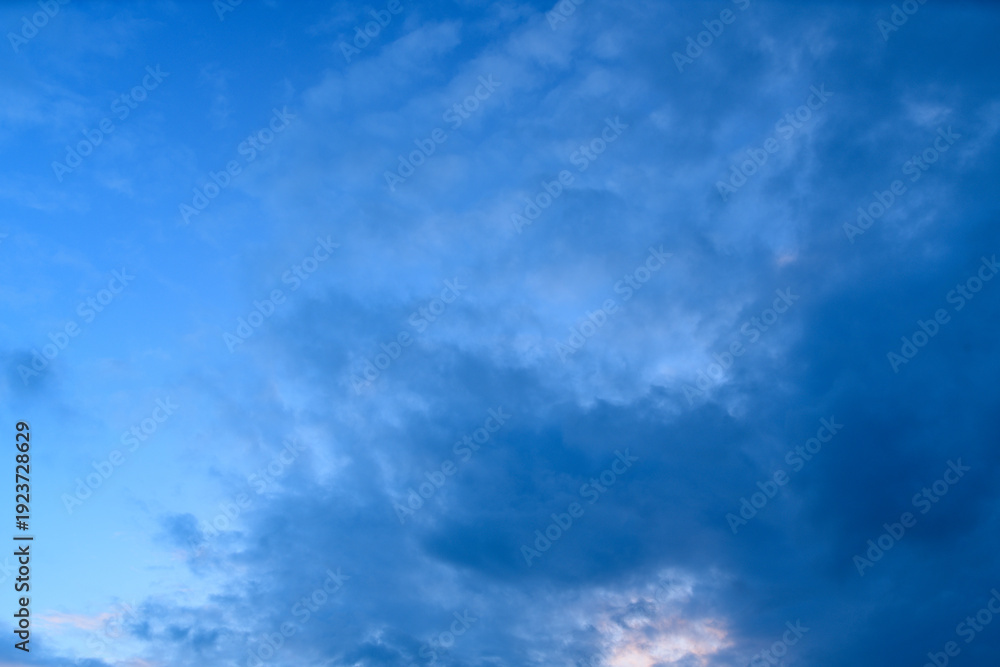 Fototapeta premium Expansive view of a deep blue evening sky filled with textured clouds, capturing the tranquil transition between day and night with soft natural gradients.