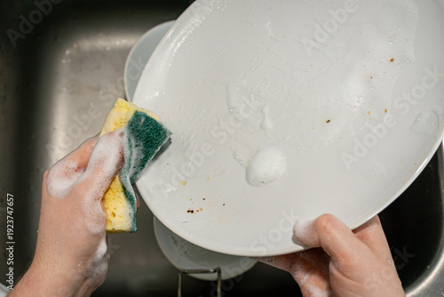 Scrubbing white plate with sponge in kitchen sink