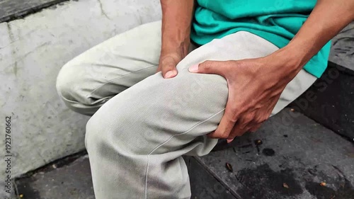 A man sits on the stairs holding his sore thigh.