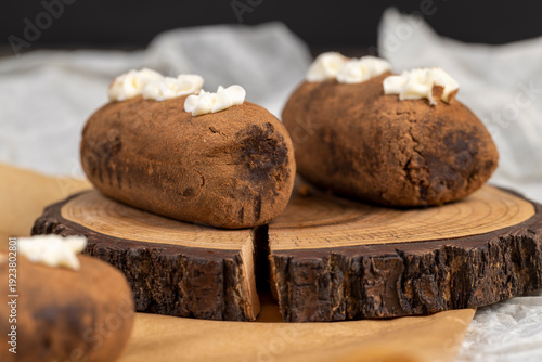 a black potato cake lies on a serving board and paper, a sweet cake made from butter and a large amount of cocoa mixed with sponge cake and cognac