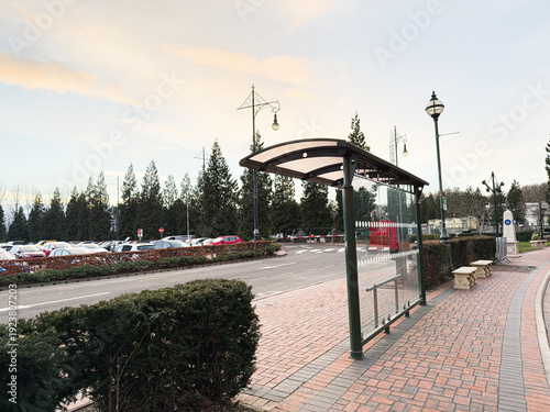 Bus stop shelter on a brick sidewalk in Manchester UK with parked cars and trees