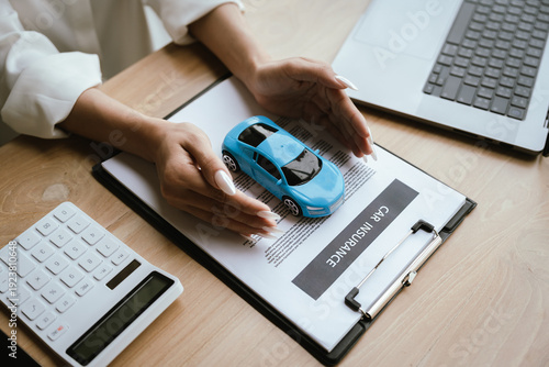 Hands protect two toy cars placed on a car insurance document, symbolizing vehicle protection, accident coverage, and auto insurance policy planning.