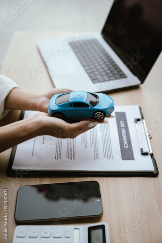 Cuadro en lienzo A woman reviews and signs a car insurance policy at her desk with a calculator, laptop, and miniature cars, representing auto coverage planning and financial protection