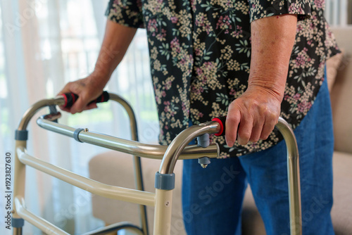 Elderly woman with a floral shirt holding a metal walker, walking indoors. Emphasizing independence and support for senior health