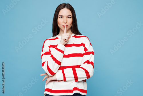 Foto Young Caucasian woman wear red striped sweatshirt casual clothes say hush be quiet with finger on lips shhh gesture isolated on plain pastel light blue background studio portrait