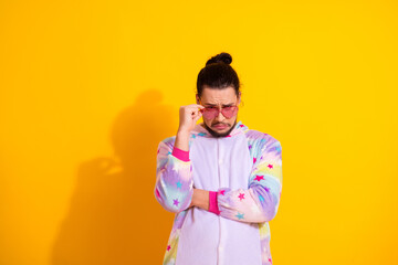 Young man wearing pastel unicorn pajama jumpsuit posing in bright yellow studio for a playful sleepwear fashion photo