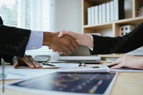 Obraz na płótnie Two business professionals shaking hands over financial reports and a calculator in an office, symbolizing successful agreement, partnership, and corporate deal closure