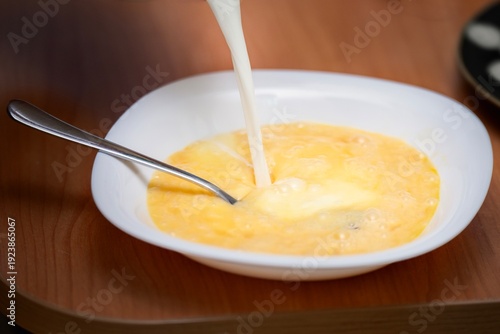 Wallpaper Mural Pouring milk into a plate with eggs and a metal fork for omelette preparation. Breakfast cooking process. Torontodigital.ca