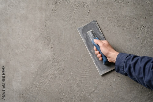 Male worker hand holding a trowel and plastering gray concrete wall.