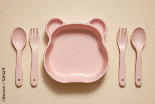 Baby feeding accessories. First safe bear shaped plate, fork, spoon, bib. Silicone tableware, cutlery set on beige neutral background. Kids dishware concept. Serving child food. Solid color backdrop.