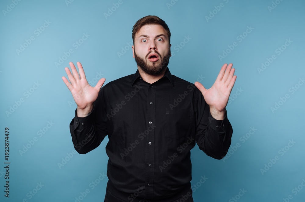 Naklejka premium Man expressing surprise in front of a blue background during an unexpected moment while dressed in black attire