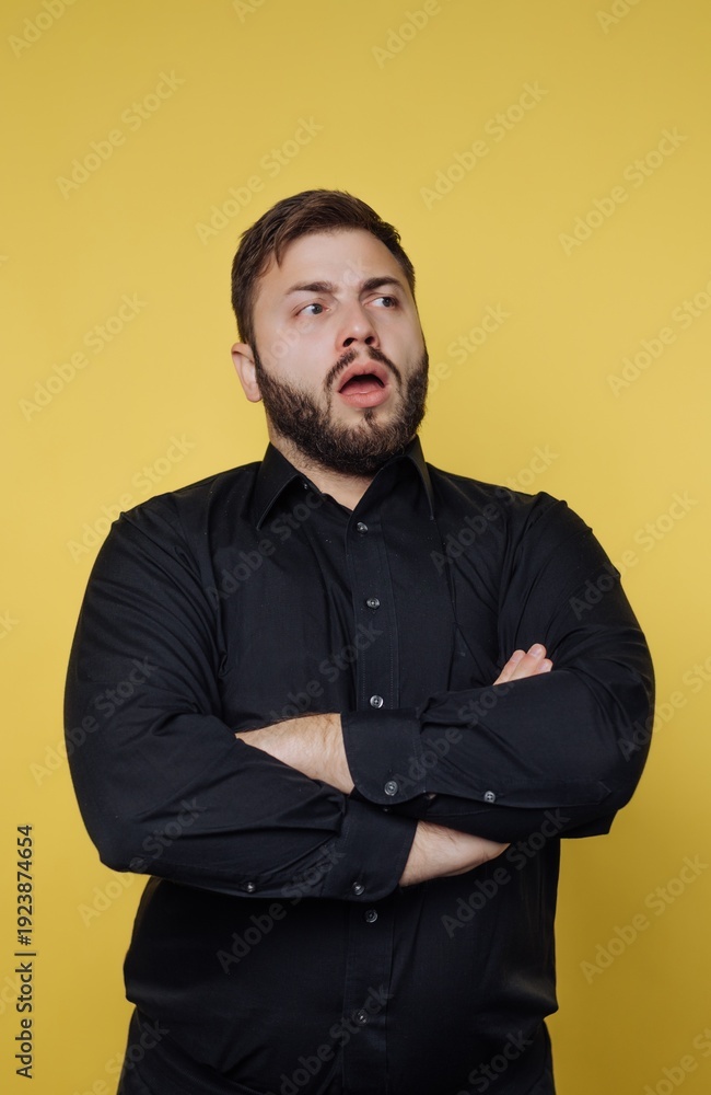 Obraz premium Surprised man with crossed arms expresses curiosity against a bold yellow backdrop in a casual setting