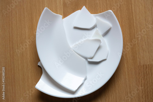 Broken plate pieces scattered on a wooden table after an accident at home during the afternoon