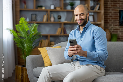 Φωτογραφία Young man sitting on a sofa in his modern living room, smiling and absorbed in h