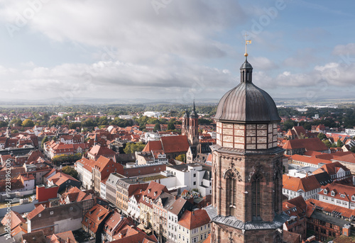 Close drone view over Goettingen (Göttingen), Germany, highlighting a historic tower above red roofs and the surrounding cityscape, with soft clouds and open sky providing copy space.