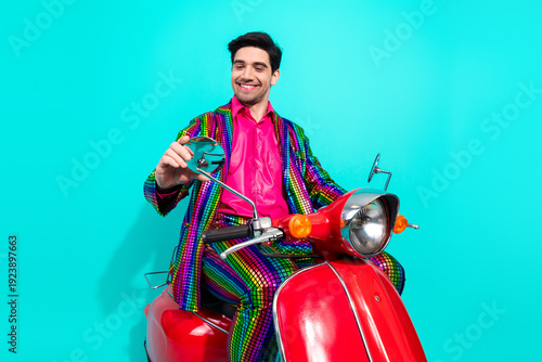 Vibrant showman in a rainbow suit smiles while riding a red scooter ready for a party or performance