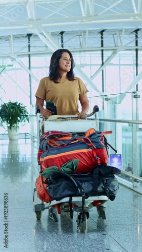 Smiling traveler woman with passport pushing luggage cart at the airport terminal