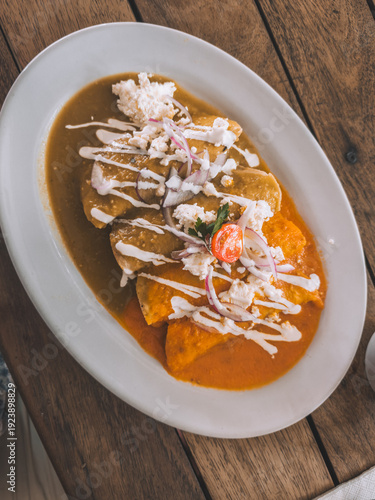 Traditional Mexican enchiladas topped with sauce, cream, cheese and red onion served on wooden table in Holbox, Mexico.
