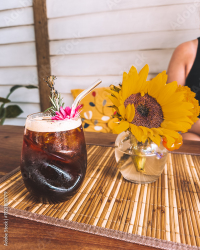 Iced coffee cocktail garnished with flower and rosemary served beside sunflower bouquet in Holbox café.