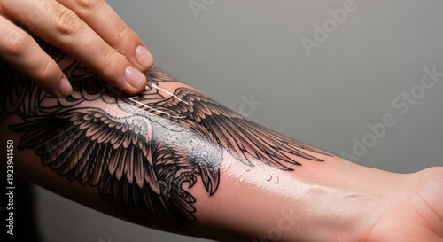 freshly tattooed forearm being treated with ointment in a caring manner against a neutral background
