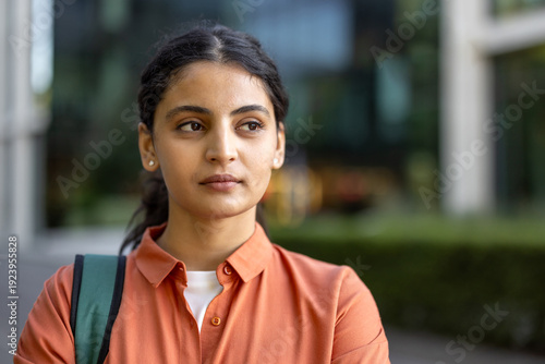 Fotografie Young indian woman standing outdoors, wearing a backpack and an orange shirt, lo