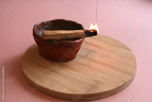 Burning Palo Santo Stick with Smoke in Clay Bowl on Wooden Tray, Minimal Pink Background

