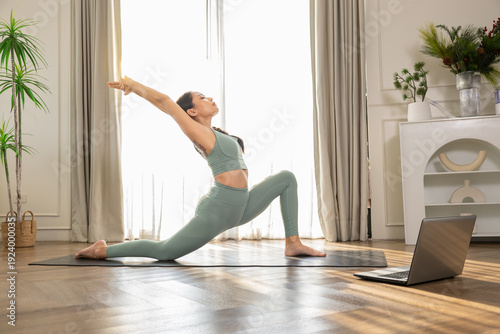 Photos Asian woman learning yoga online via laptop stretching body at home living room