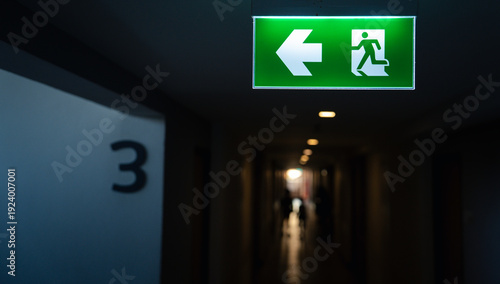 Quadro su tela Emergency exit sign with running man icon and directional arrow in dark corridor