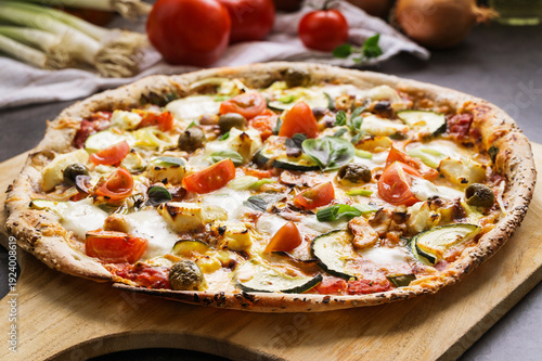 Fresh vegetarian pizza with mozzarella, tomatoes and zucchini on wooden board