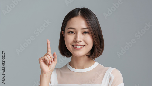 Naklejka 東アジアの二十代女性が人差し指を立てて微笑む、スタジオで伝えるワンポイント