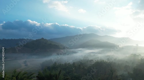 VDO Aerial view of Morning Mist Over Mountain Village with Sun Rays and Tropical Forest Landscape, Thailand creating a peaceful and atmospheric scene.
