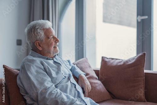 Photos A retired man rests on a sofa indoors, staring out the window with a relaxed fac