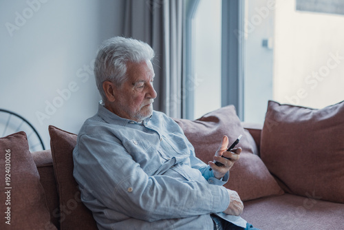 Tableau sur toile Concerned senior man sit on sofa at home holds smartphone, staring at screen, le