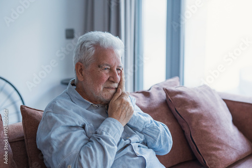 Foto A senior man rests on the couch at home touching his jaw with a pained expressio