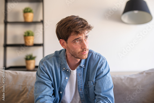Photography A lonely young man sits on the couch at home, lost in thought and struggling wit