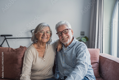 Obraz na plátně A happy older married couple stands together at home, laughing and hugging with