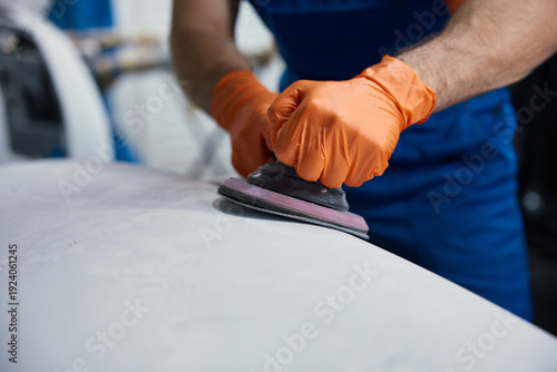 Cuadro en lienzo Worker sanding car surface with orbital sander - orange gloves in auto body work