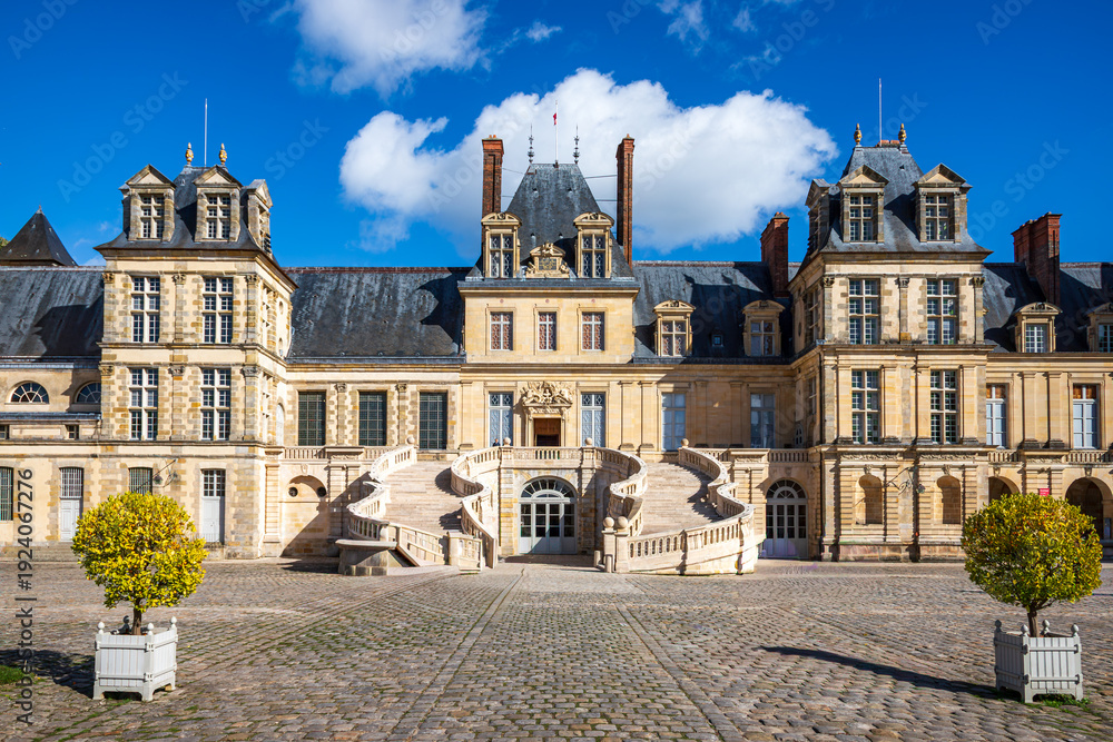 Obraz premium Centered architectural view of Château de Fontainebleau in France highlighting the iconic horseshoe staircase, ornate entrance, and symmetrical historic façade under bright blue sky, UNESCO Site